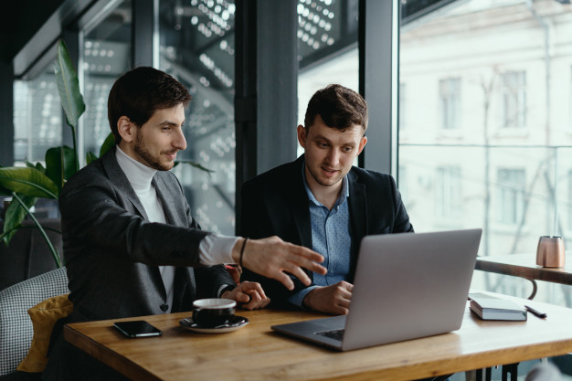 two-businessmen-pointing-laptop-screen-while-discussing_158595-5324