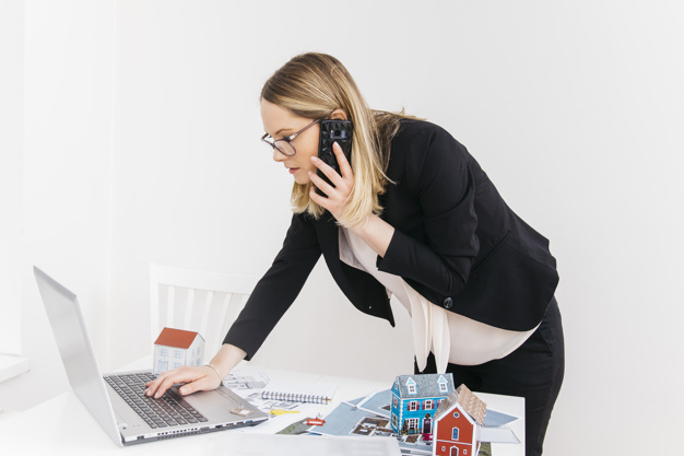 young-attractive-woman-talking-cellphone-while-working-laptop-real-estate-office_23-2148182947